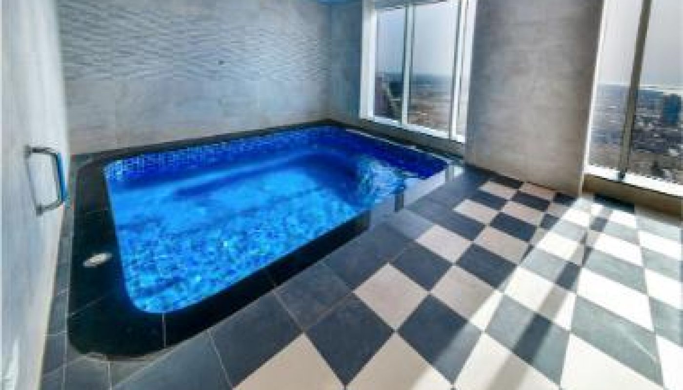 Indoor pool in a modern room with large windows, gray walls, and black-and-white checkered tile floor; cityscape visible outside.