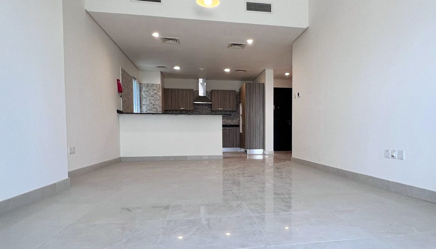 Unfurnished apartment with tiled floors, white walls, open kitchen, and modern lighting fixture, viewed from the living area towards the kitchen.