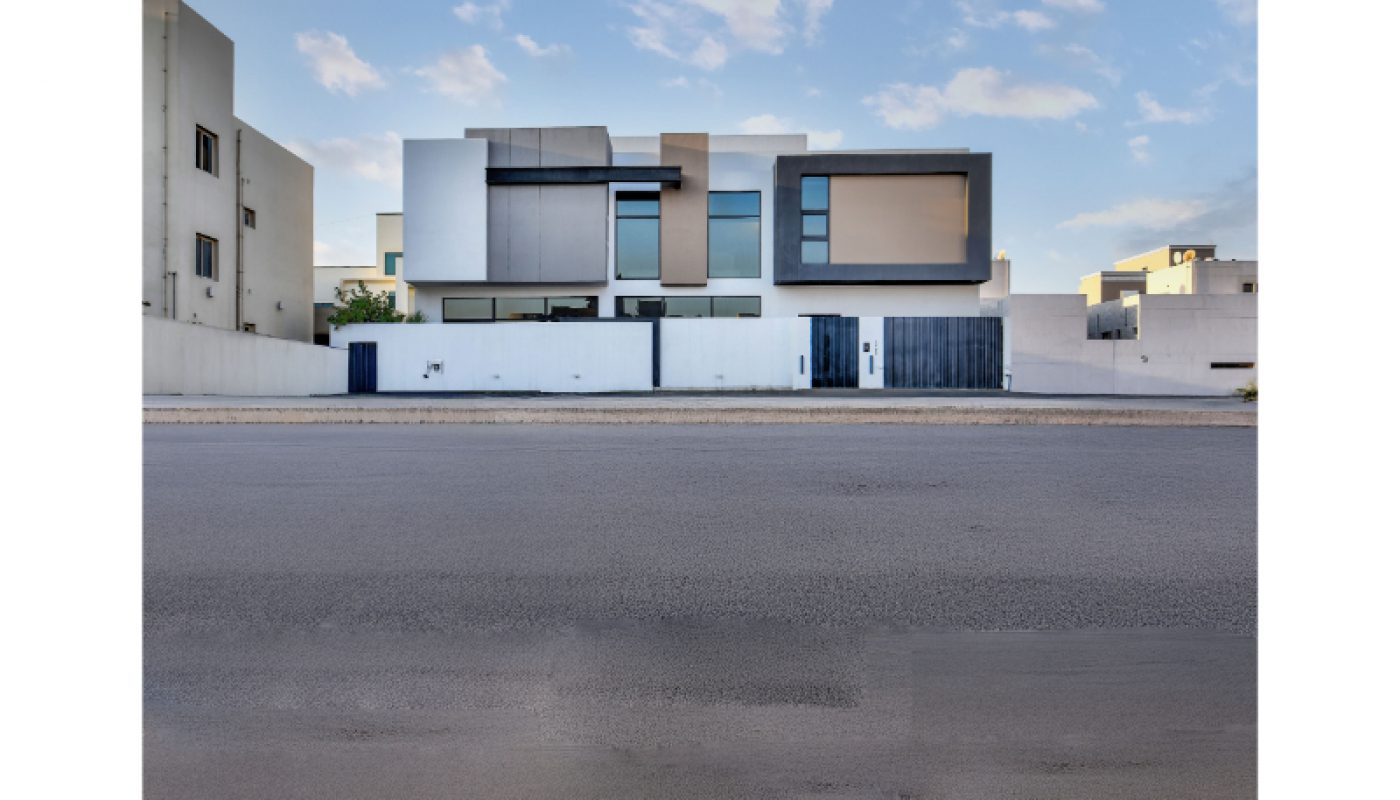 Modern two-story house with a minimalist geometric design, large windows, and a flat roof, set against a clear sky and surrounded by other contemporary buildings.