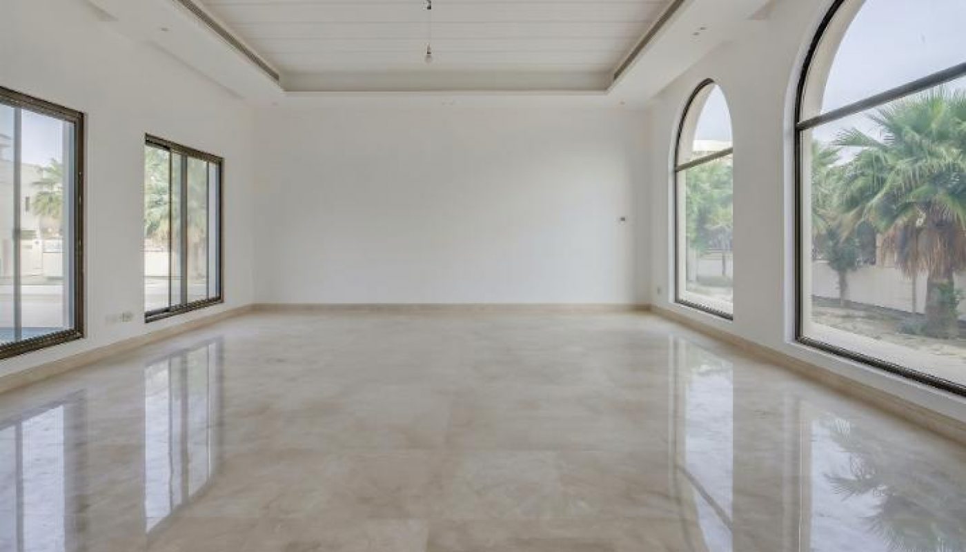 Spacious empty room with polished marble floor, white walls, high ceiling, and large windows including two arched ones that overlook greenery outside.