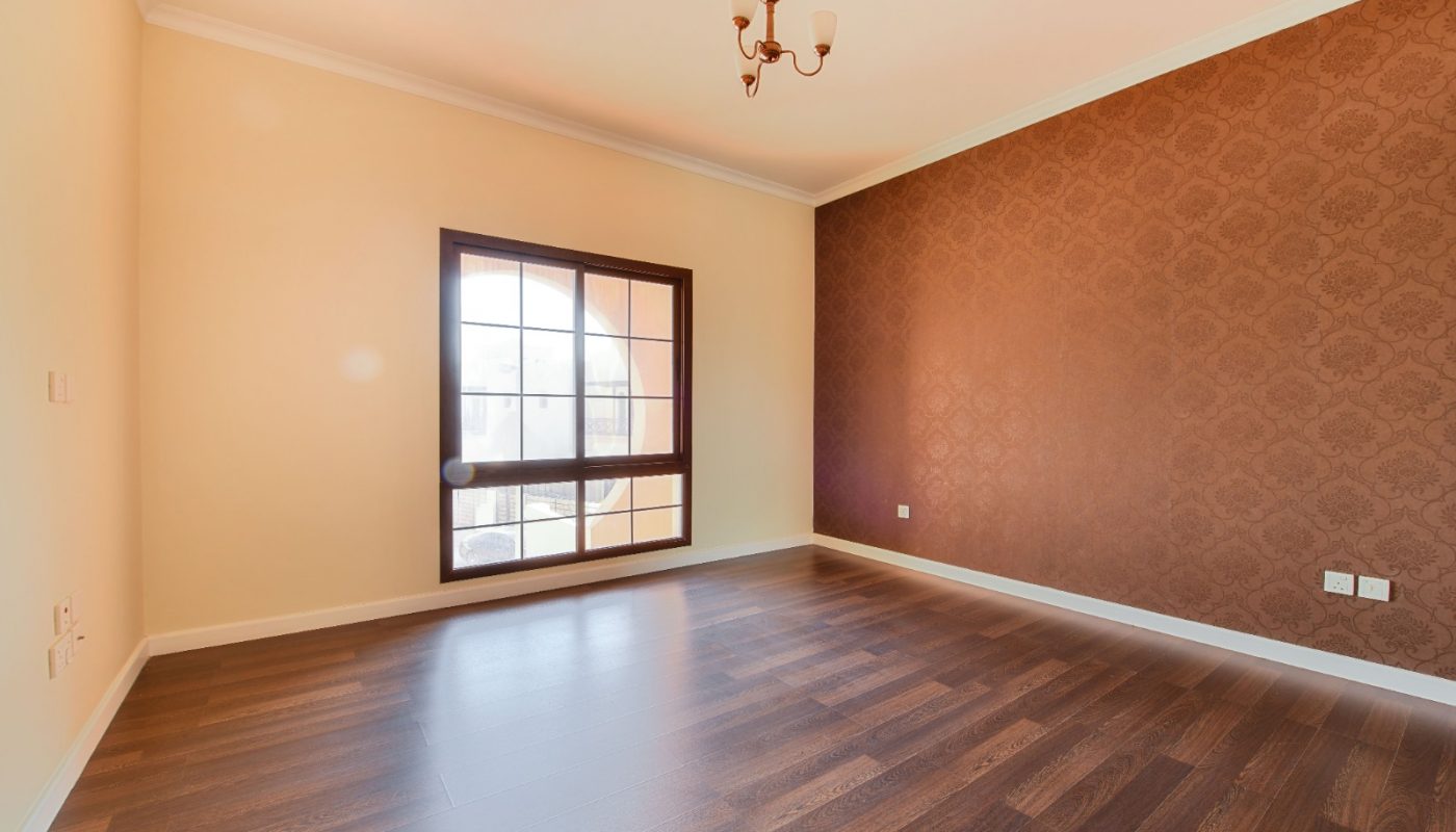 Empty room with dark wood flooring, a patterned accent wall, a window with an arched frame, and a small ceiling light fixture.