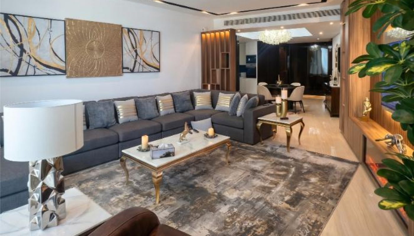 Modern living room with a large gray sectional sofa, brown armchair, coffee table, abstract artwork, and decorative plants, featuring neutral tones and contemporary decor.