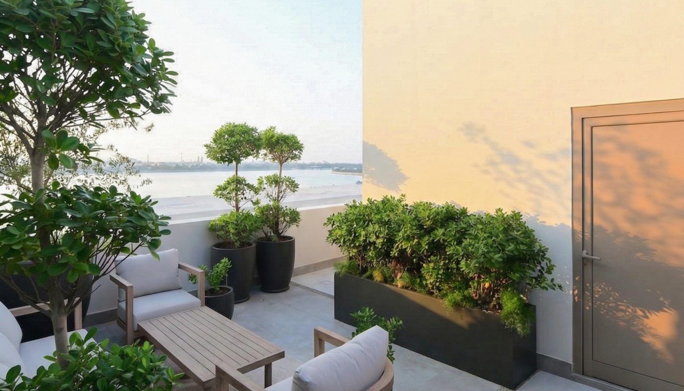 Rooftop patio with cushioned chairs, a wooden table, potted plants, and a beige wall under clear blue sky.