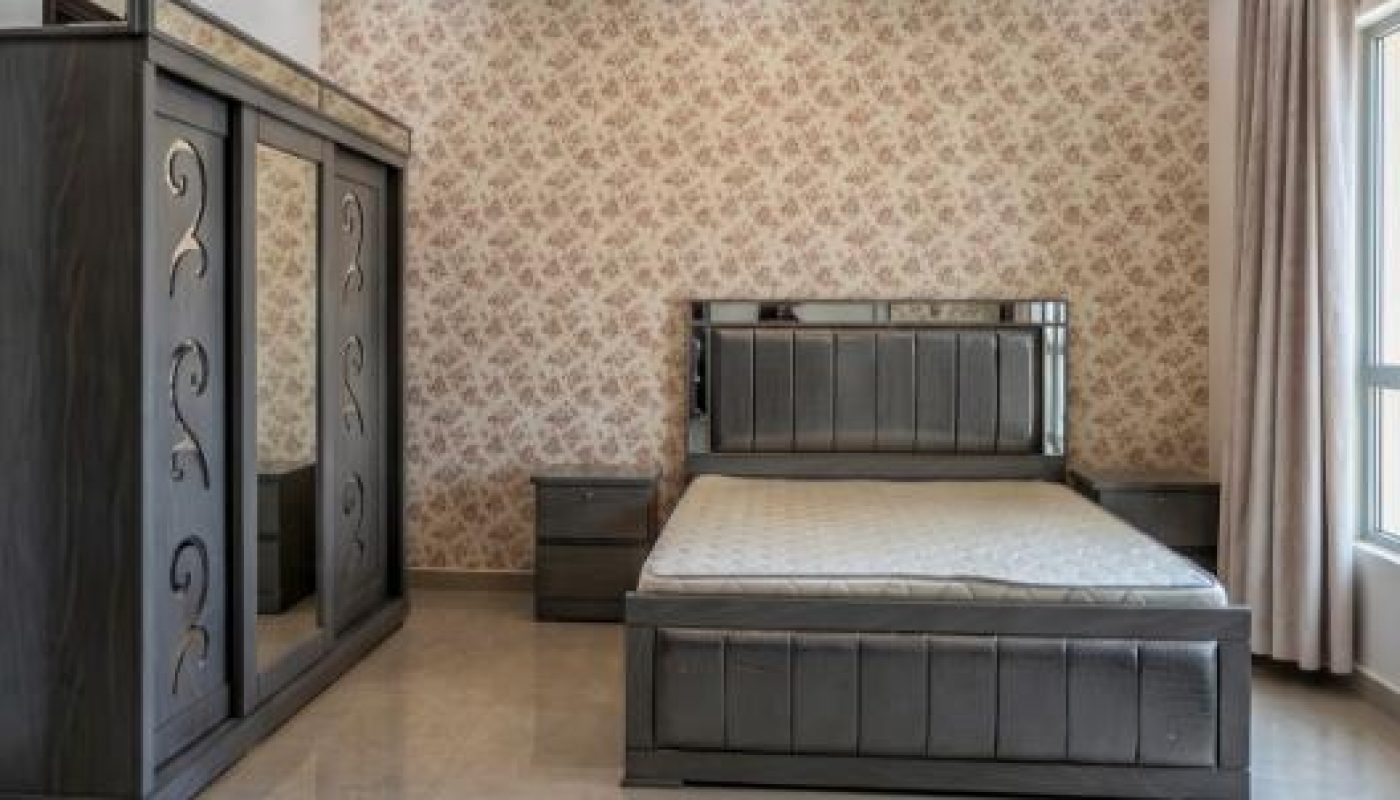 A modern bedroom with a double bed, two bedside tables, a large wardrobe with mirrors, patterned wallpaper, and a window with curtains.