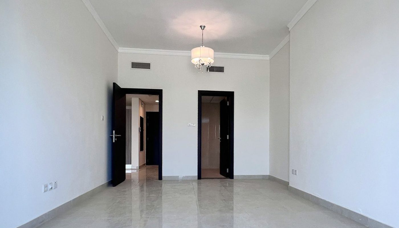A spacious, empty room with white walls, tiled floor, two ceiling lights, and two open black doors leading to adjacent areas.
