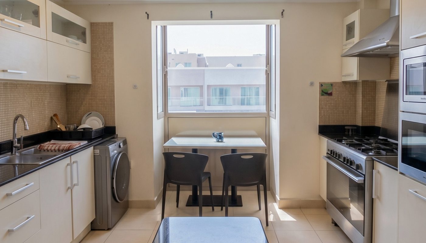 Modern kitchen with white cabinets, black countertops, stainless steel appliances, and a small dining table for two by a window.