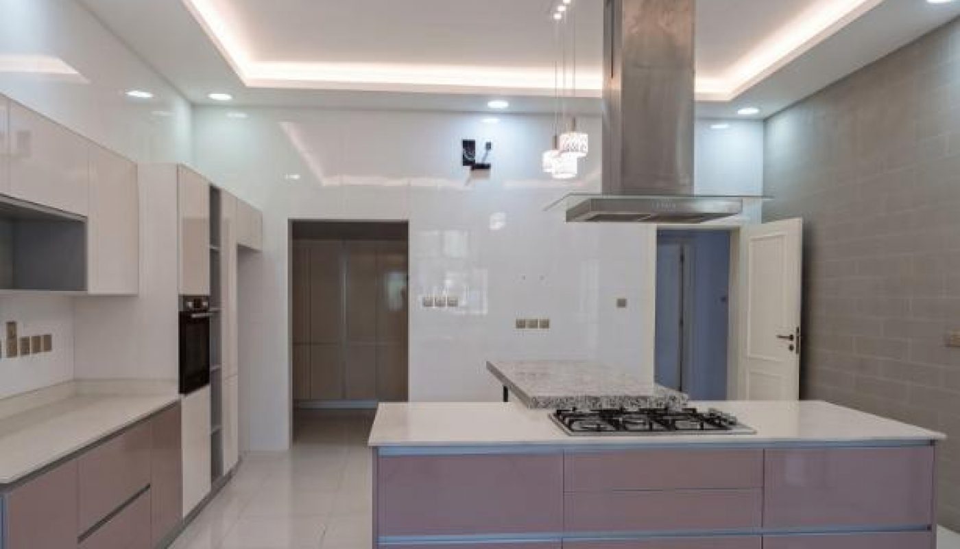 Modern kitchen with light pink cabinets, a central island with a gas stove, built-in appliances, tile flooring, and recessed ceiling lights.