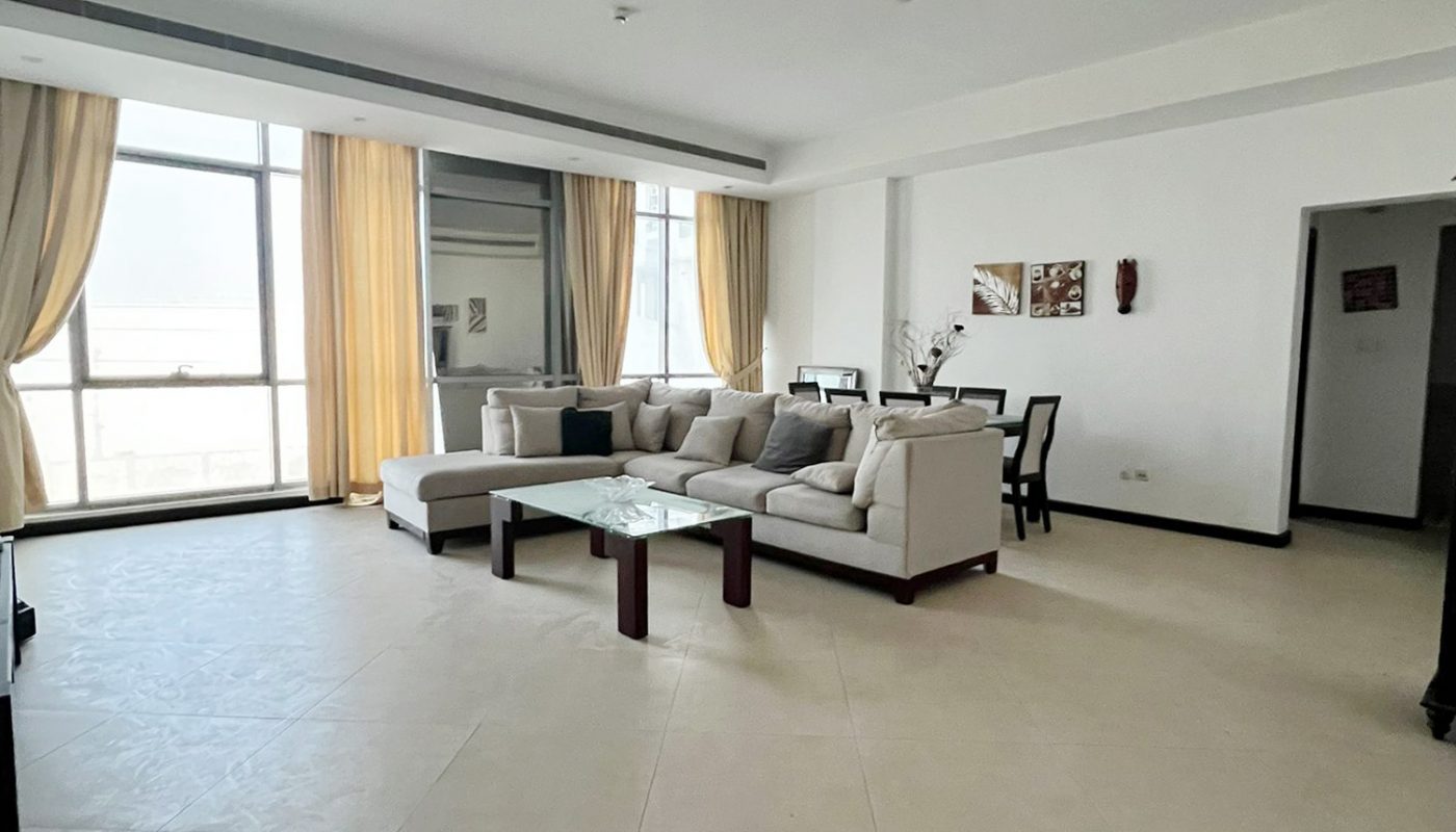 Spacious living room with large windows, cream tile floors, a sectional sofa, a coffee table, and dining area with chairs and wall art.
