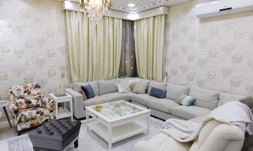 A luxury living room with white furniture and a chandelier in a 3BR apartment in Isa Town.