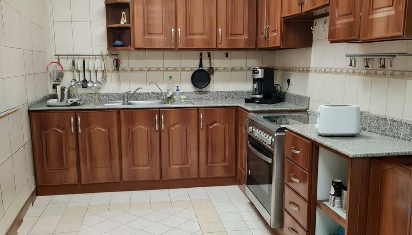 Modern kitchen with wooden cabinets, granite countertops, tiled floor, toaster, gas stove, coffee maker, and various utensils. The space appears clean and organized.