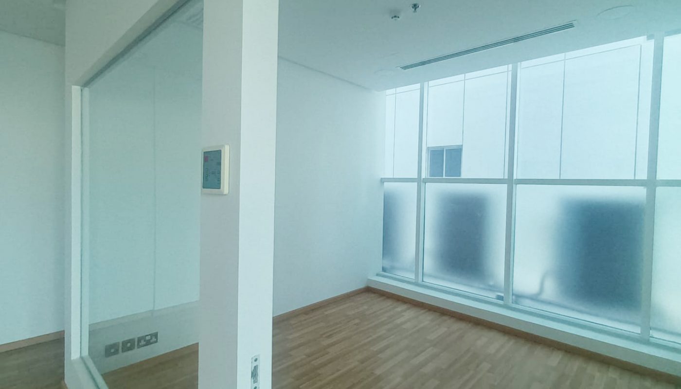 Empty room with wooden flooring, large frosted windows, white walls, and a glass partition separating two areas.
