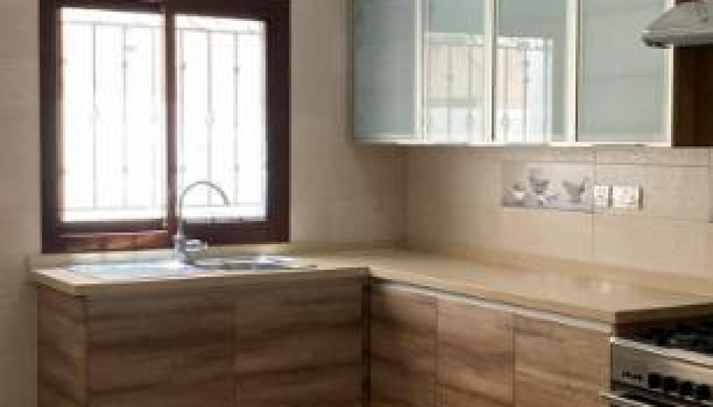 Modern kitchen with wood cabinets, beige countertops, a stove, glass-fronted upper cabinets, and a window above the sink.