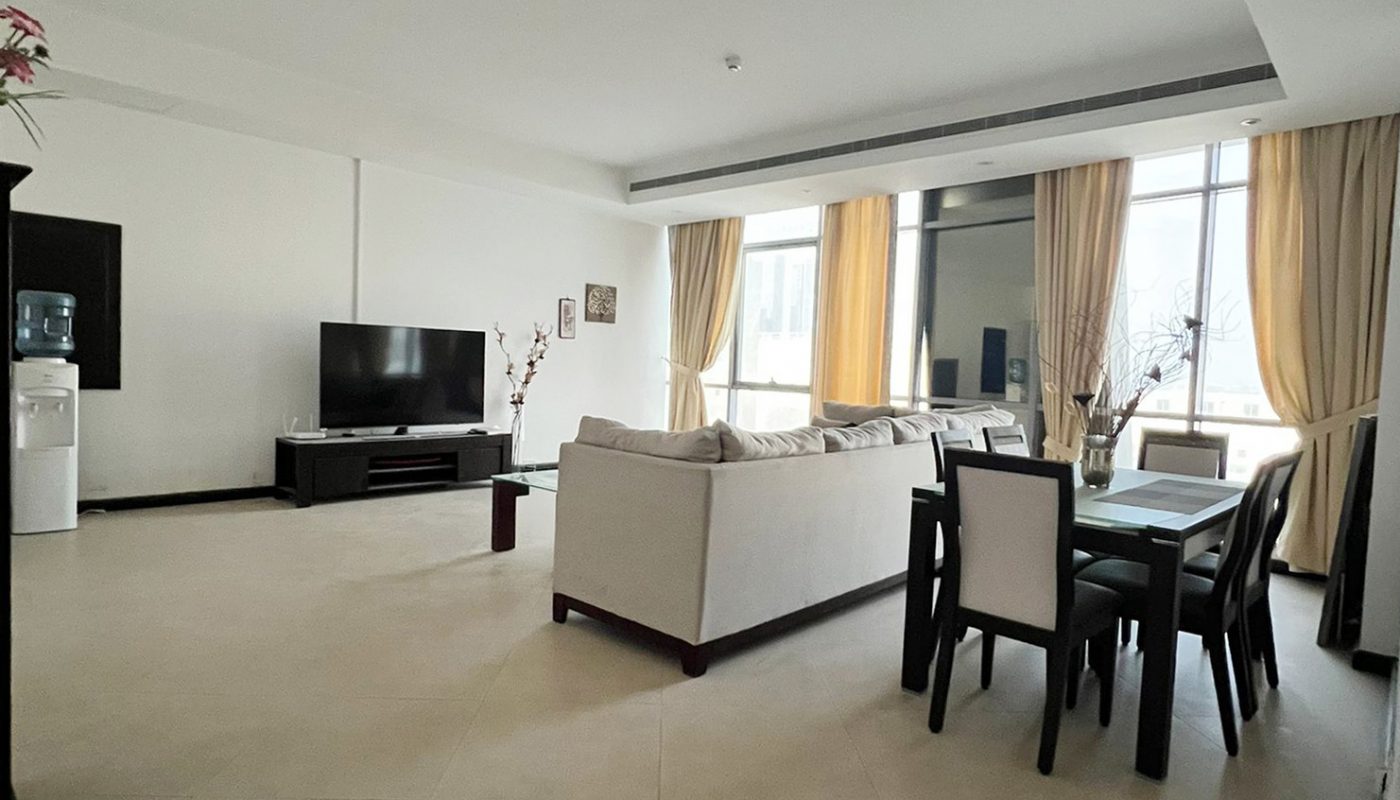 Spacious living and dining area with tiled floor, white sofa, dark dining table, TV, water dispenser, large windows, and yellow curtains.