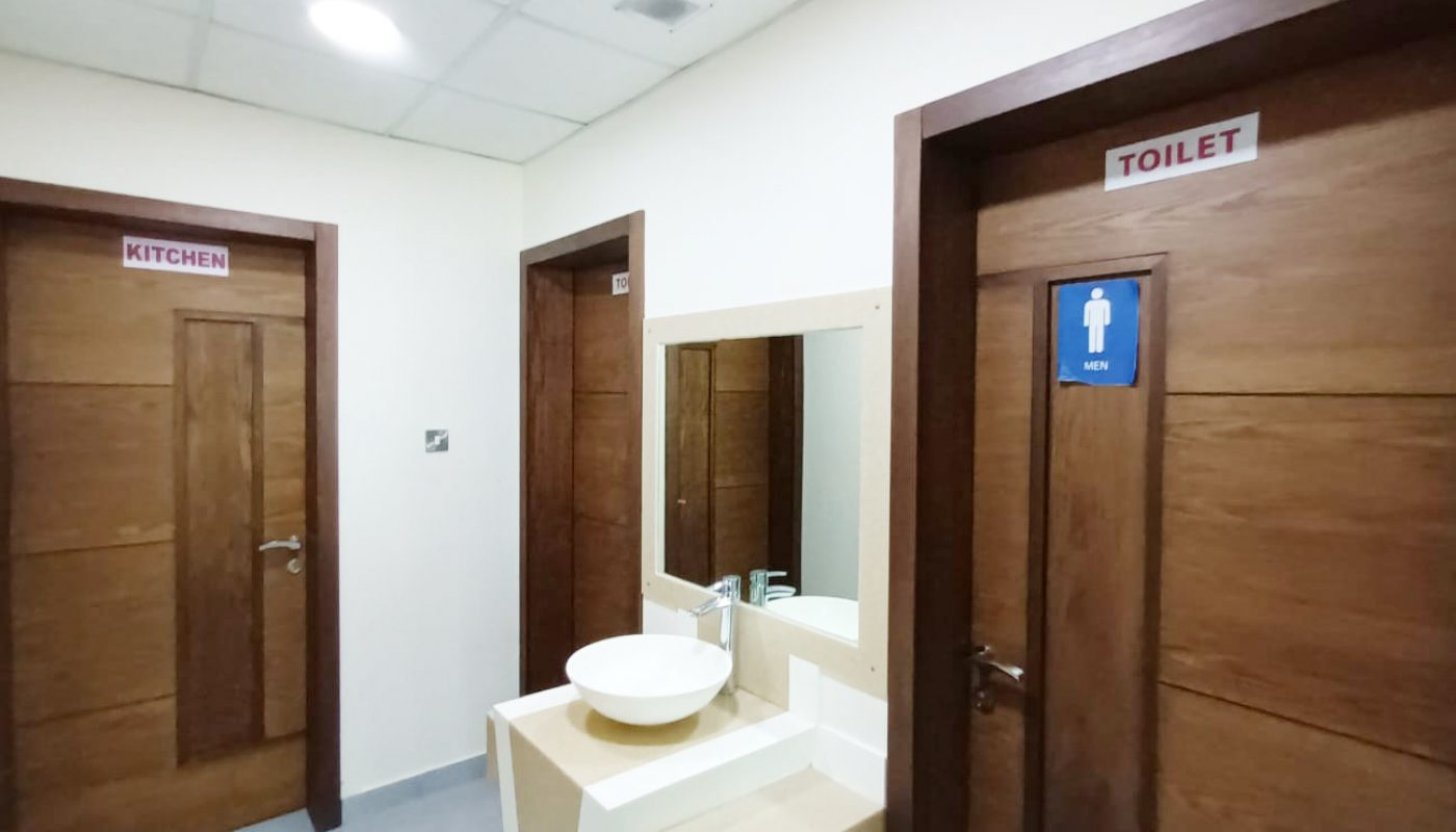 A hallway with three wooden doors labeled “KITCHEN,” “TOILET,” and one unmarked; a sink with a mirror is positioned between the doors.