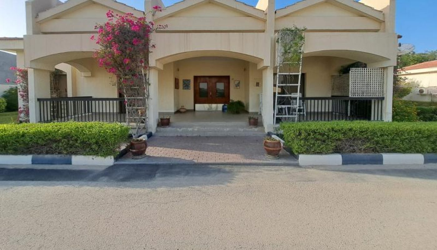 Single-story beige house with two front porches, potted plants, a ladder, and a clear blue sky above.