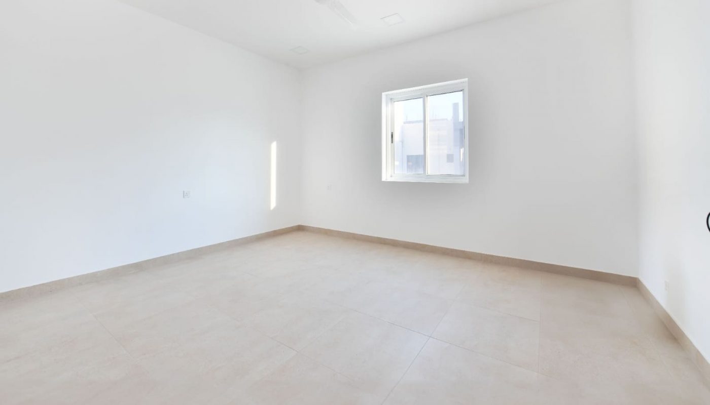 Empty room with white walls, beige tiled floor, a ceiling fan, and a single window letting in natural light.
