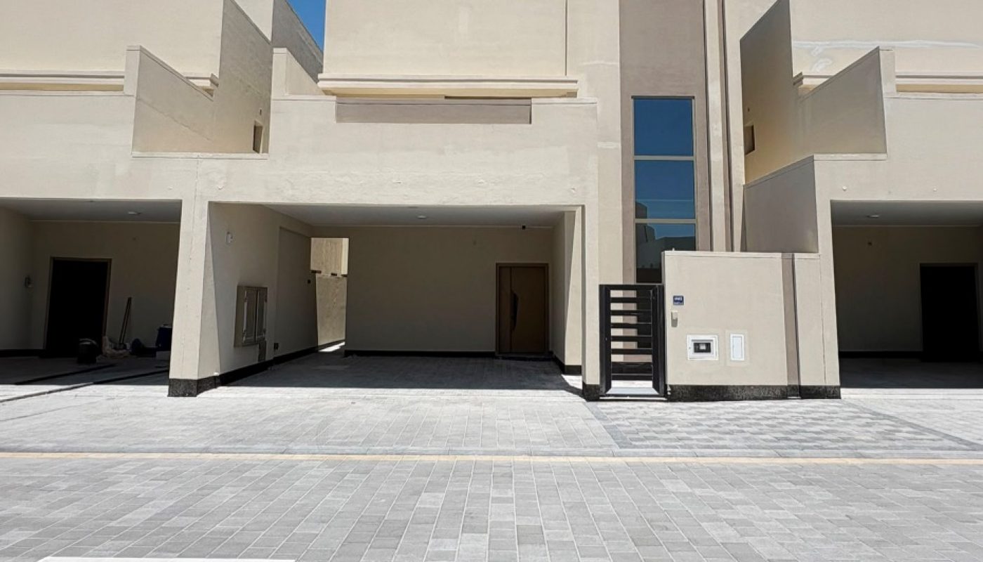 Modern beige townhouse with two covered parking spaces, flat roof, and geometric design, set against a clear blue sky.
