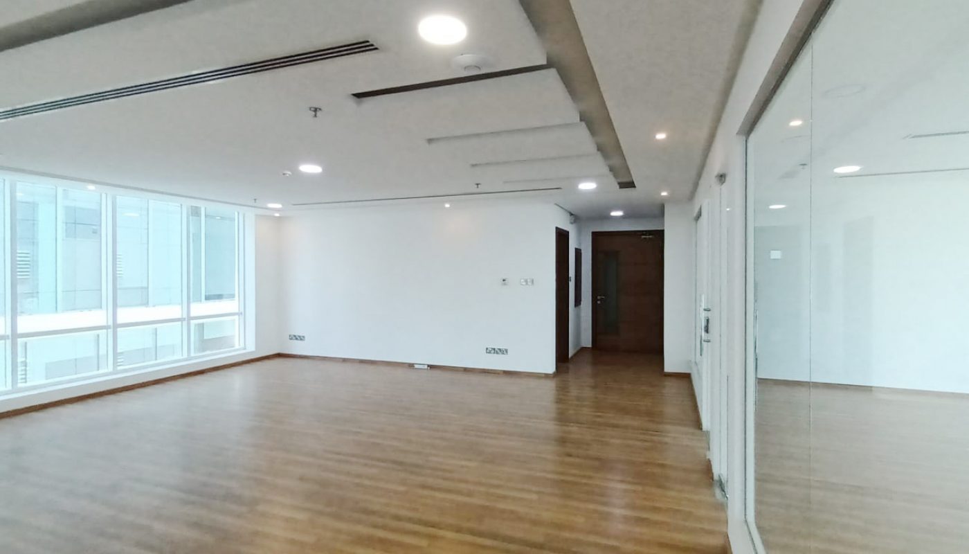 Spacious, empty room with wood flooring, white walls, ceiling lights, large windows on the left, and a glass wall on the right.