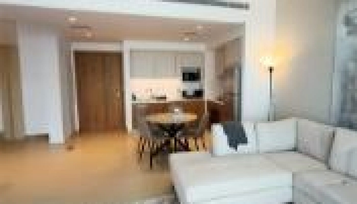 Modern open-plan living room and kitchen with a white sectional sofa, round dining table, floor lamp, and minimalist decor.