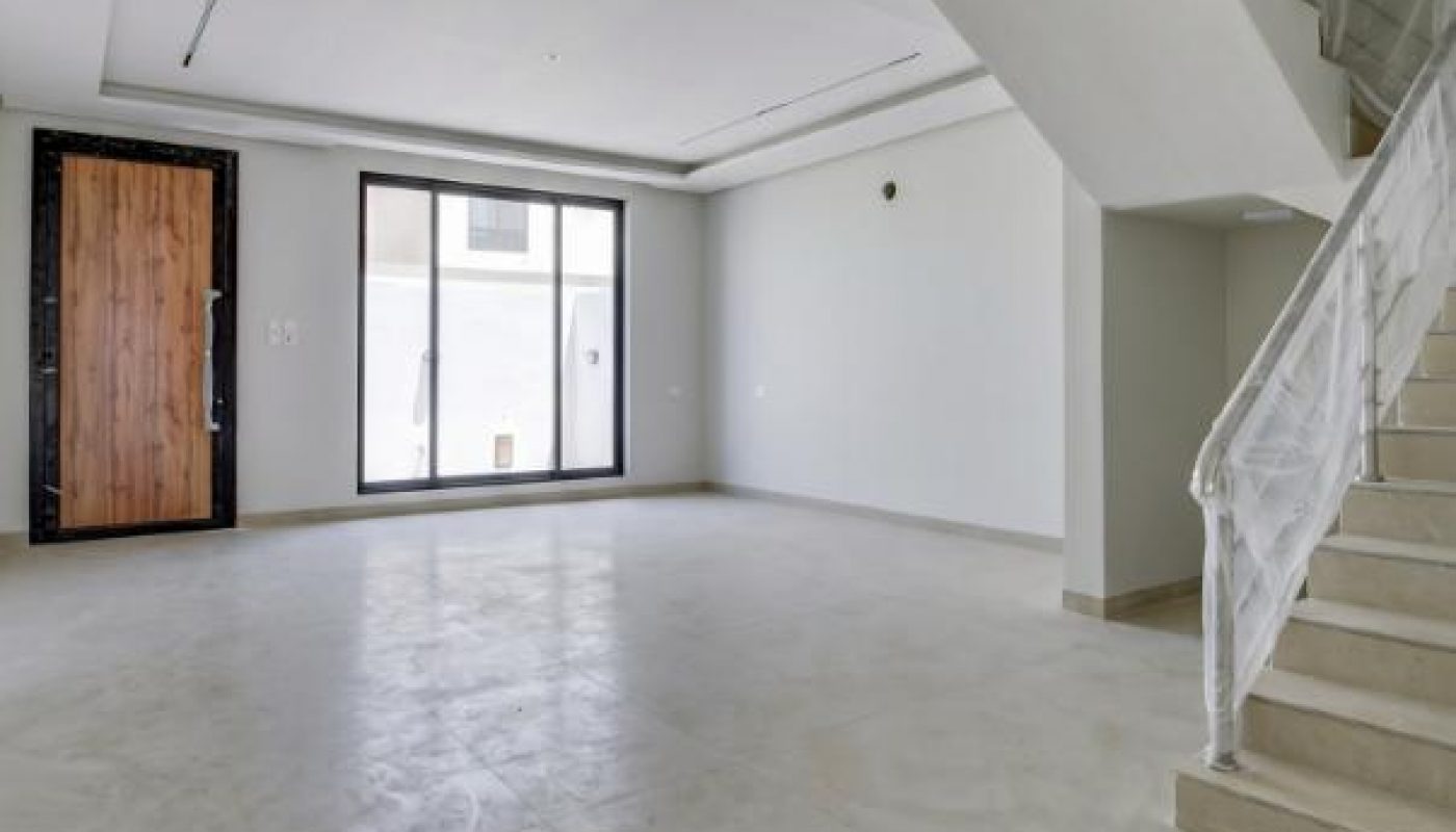 Interior view of a modern empty room with beige tiled floors, a wooden door, a large window, and a white staircase.