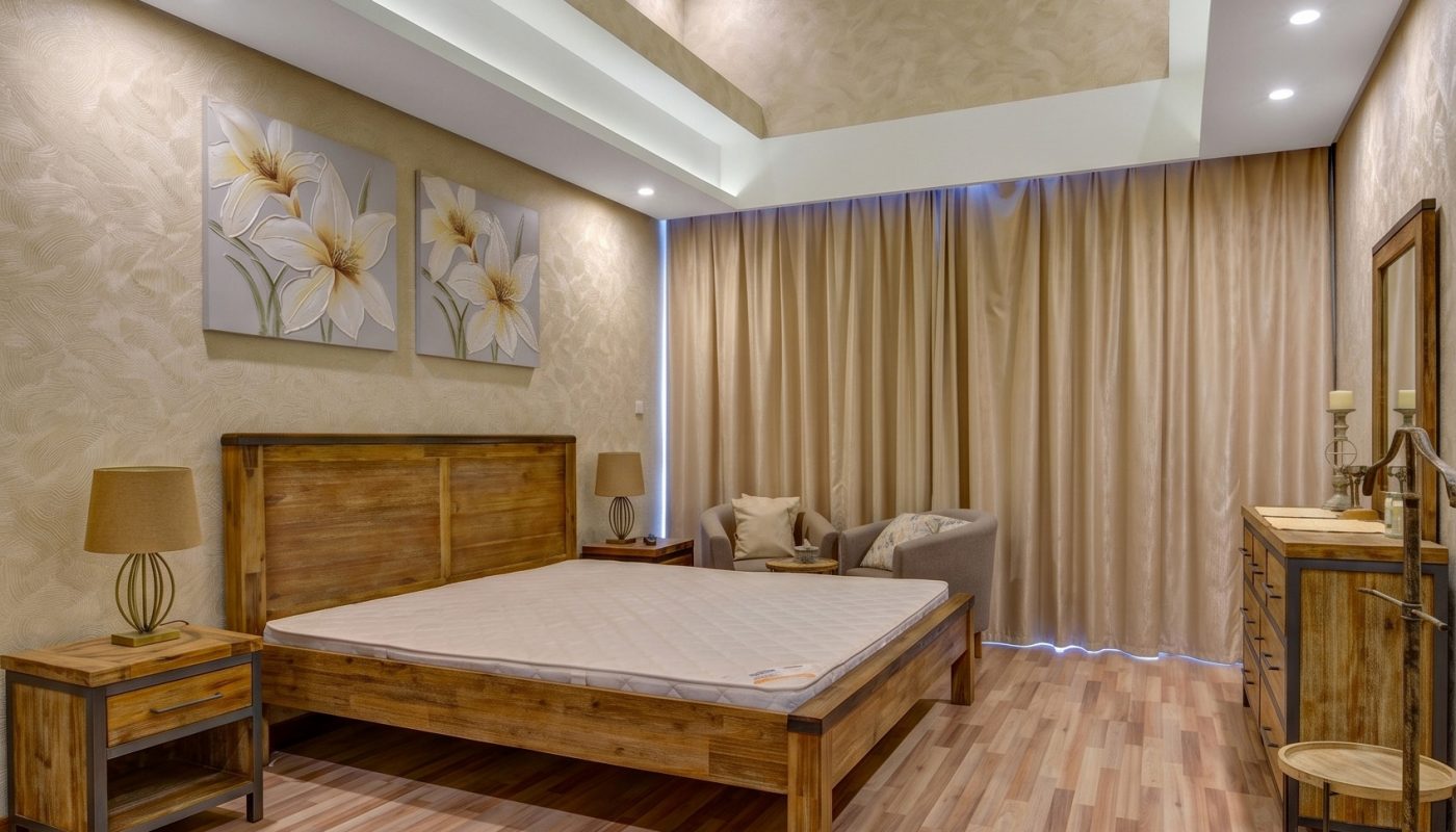 Modern bedroom with wooden furniture, a large bed, artwork on the wall, beige curtains, and a decorative ceiling with recessed lighting.