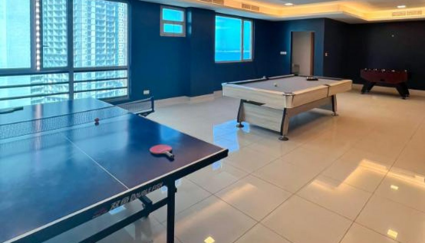 Game room with a ping pong table, pool table, and foosball table on a glossy tiled floor, with large windows and ceiling lights.