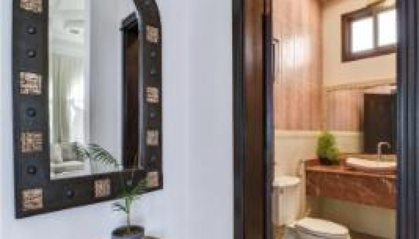 Small entry area with a decorative mirror and potted plant on a table, next to an open door leading to a bathroom with a toilet and sink.