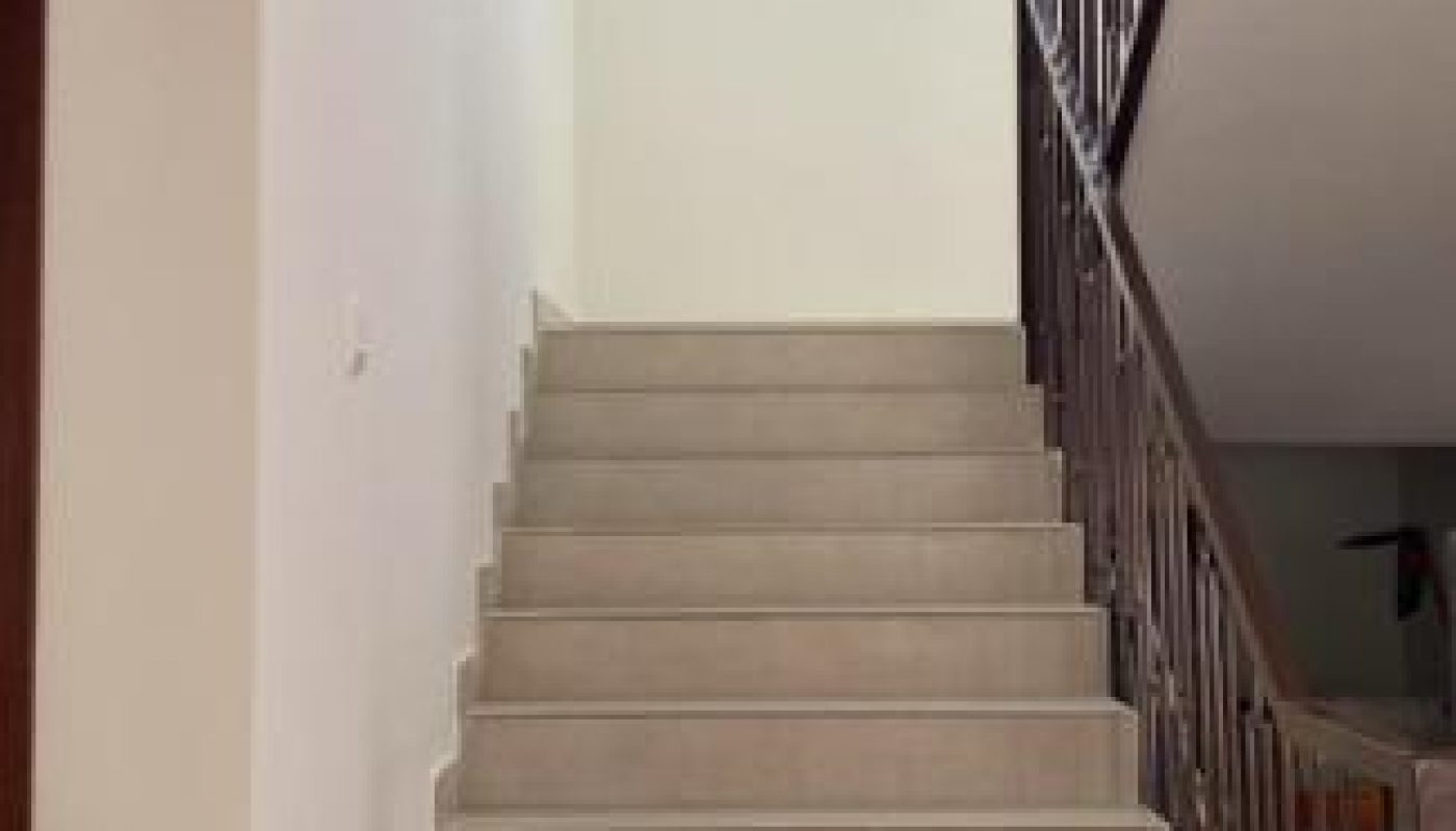A beige staircase with metal railings leads up to a landing with a large window, allowing natural light into the space.