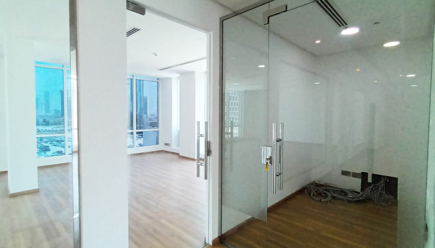 Modern office interior with glass doors, wooden flooring, large windows, city view, and a coiled cable on the floor near power outlets.
