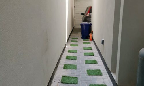 A luxurious villa hallway with green grass and a parked car.