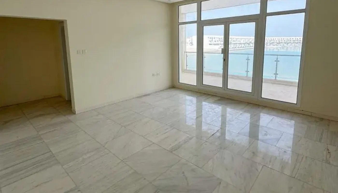 Empty room with marble flooring, large windows, glass doors, balcony with a view of water, ceiling air conditioning unit, and beige walls.