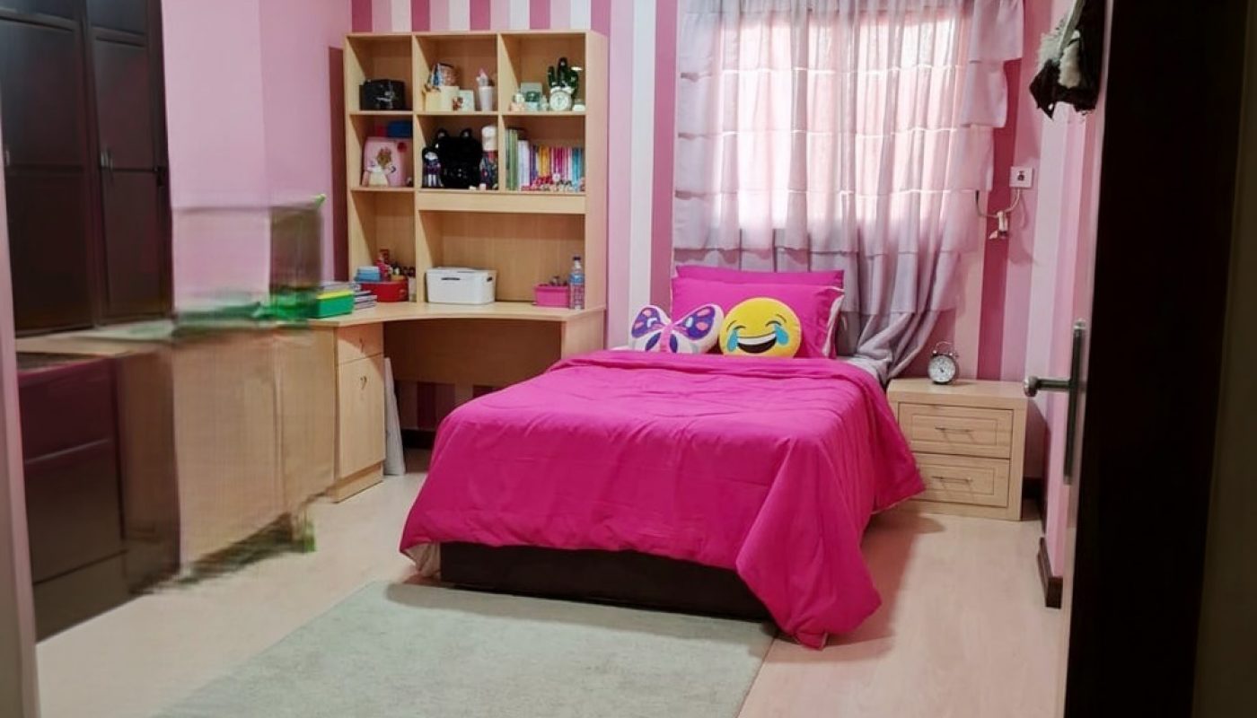 A neatly organized pink bedroom with a single bed, emoji pillows, a wooden desk, shelves, a wardrobe, and striped wallpaper.