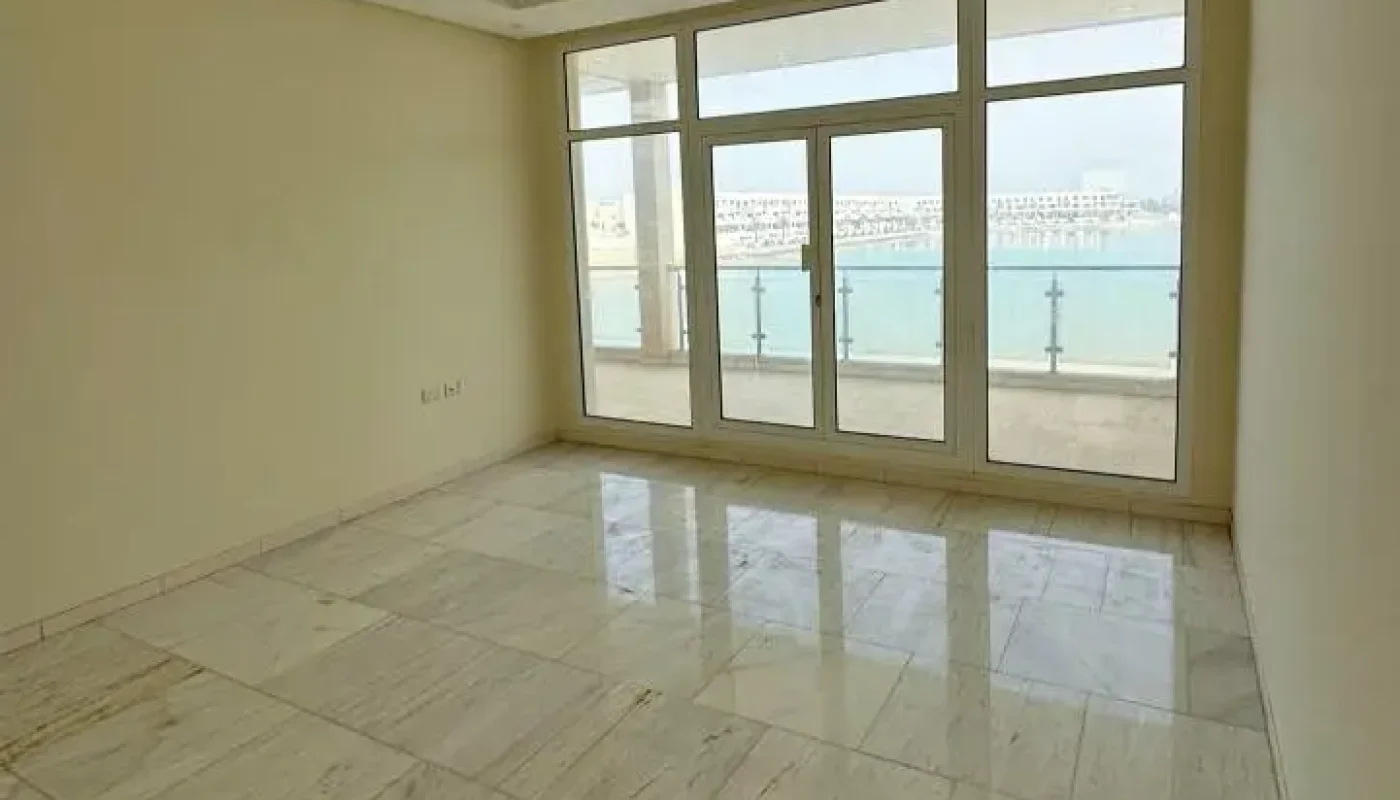 Empty room with marble floor, beige walls, ceiling air conditioning unit, and large windows overlooking a body of water with buildings in the distance.