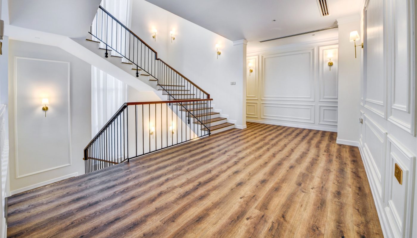 Spacious interior with wood flooring, white paneled walls, wall sconces, and a staircase with a black railing along the left side.