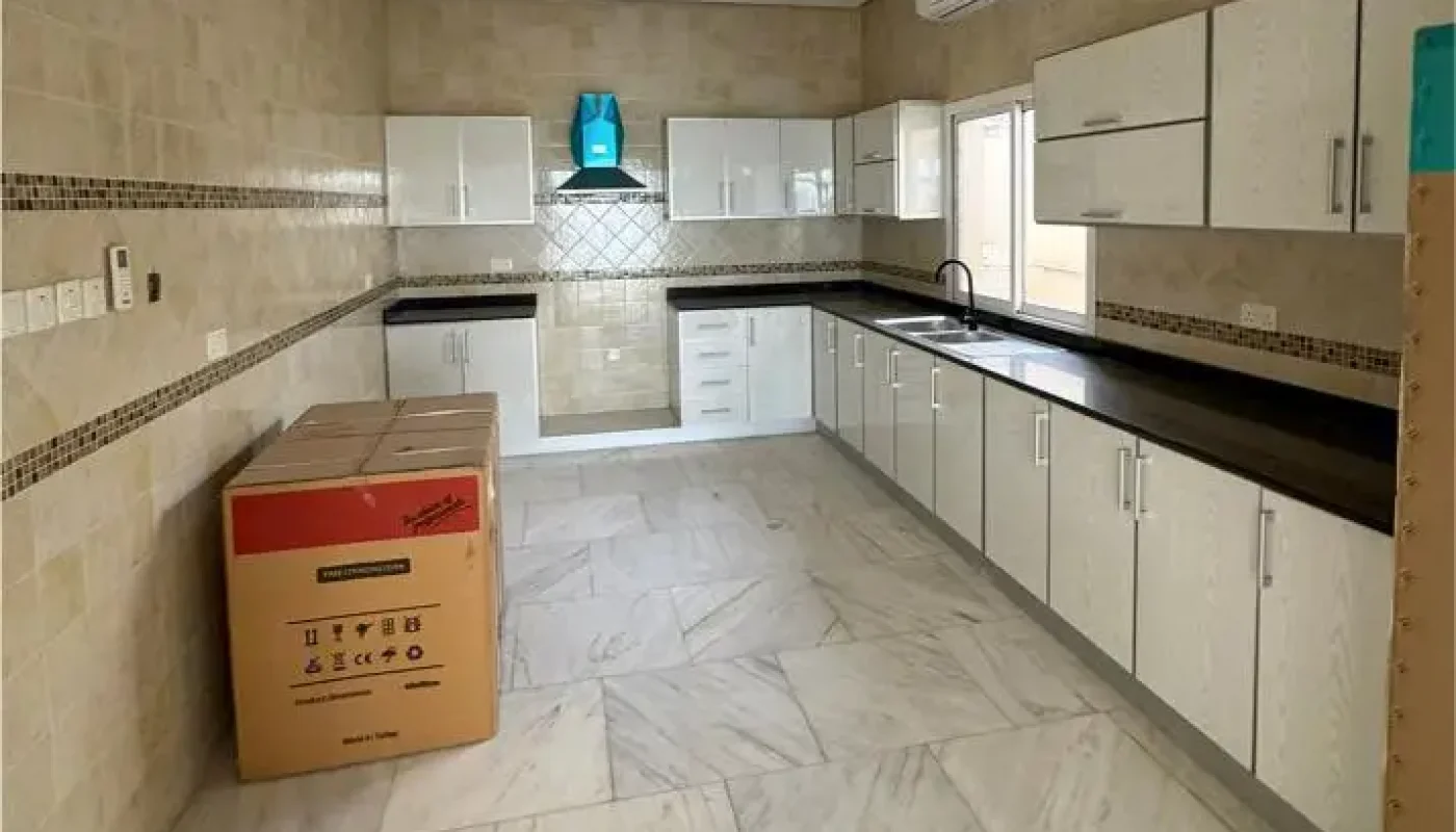 Spacious kitchen with white cabinets, marble floor, tiled walls, a window, an air conditioner, and a large cardboard box on the left side of the room.