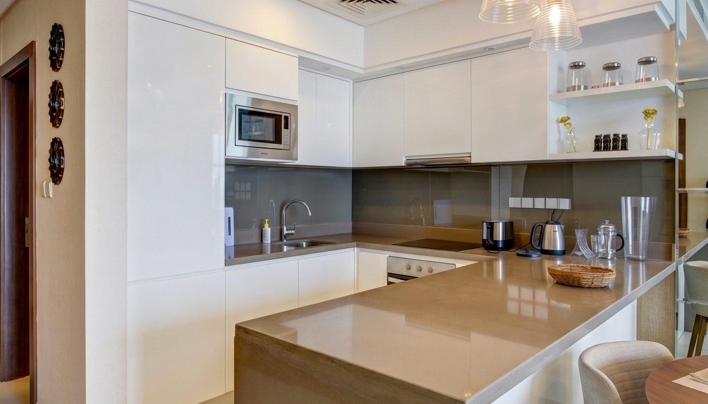Modern kitchen with white cabinets, beige countertops, built-in appliances, pendant lighting, and a dining area with a round table and upholstered chair.