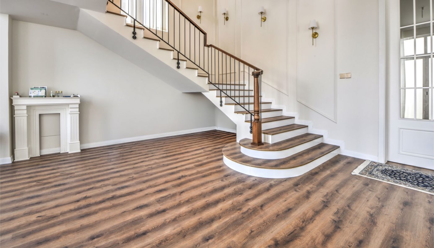 Spacious room with wood flooring, a staircase with a metal railing, white walls, a fireplace, and a door with glass panels.