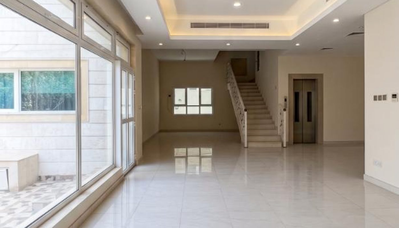 Spacious, empty living room with large windows, white tile floors, recessed ceiling lights, a staircase, and an elevator.
