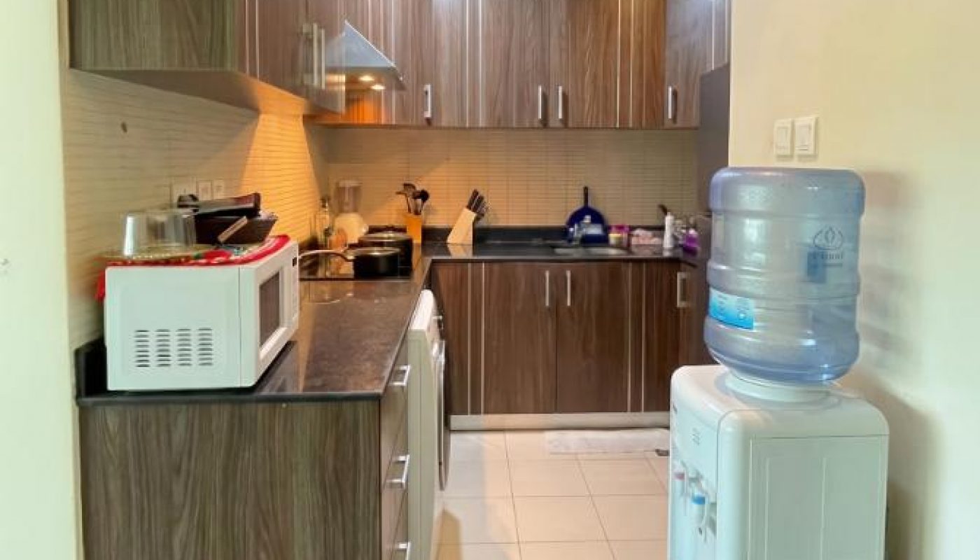 Modern kitchen with wooden cabinets, microwave, stove, countertop appliances, and a water dispenser on a tiled floor.
