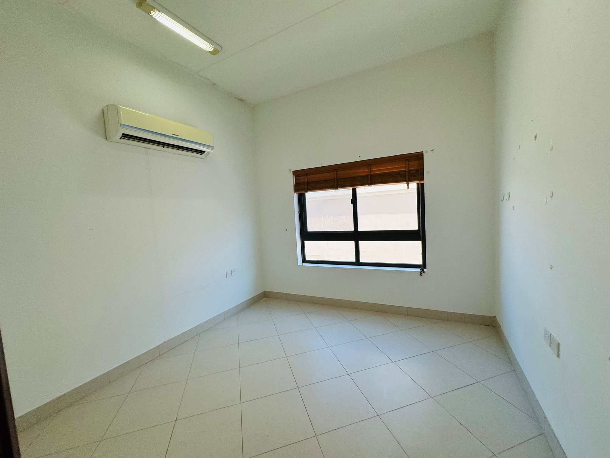 Empty room with white walls, a tile floor, a window with a wooden blind, and an air conditioning unit mounted on the wall.