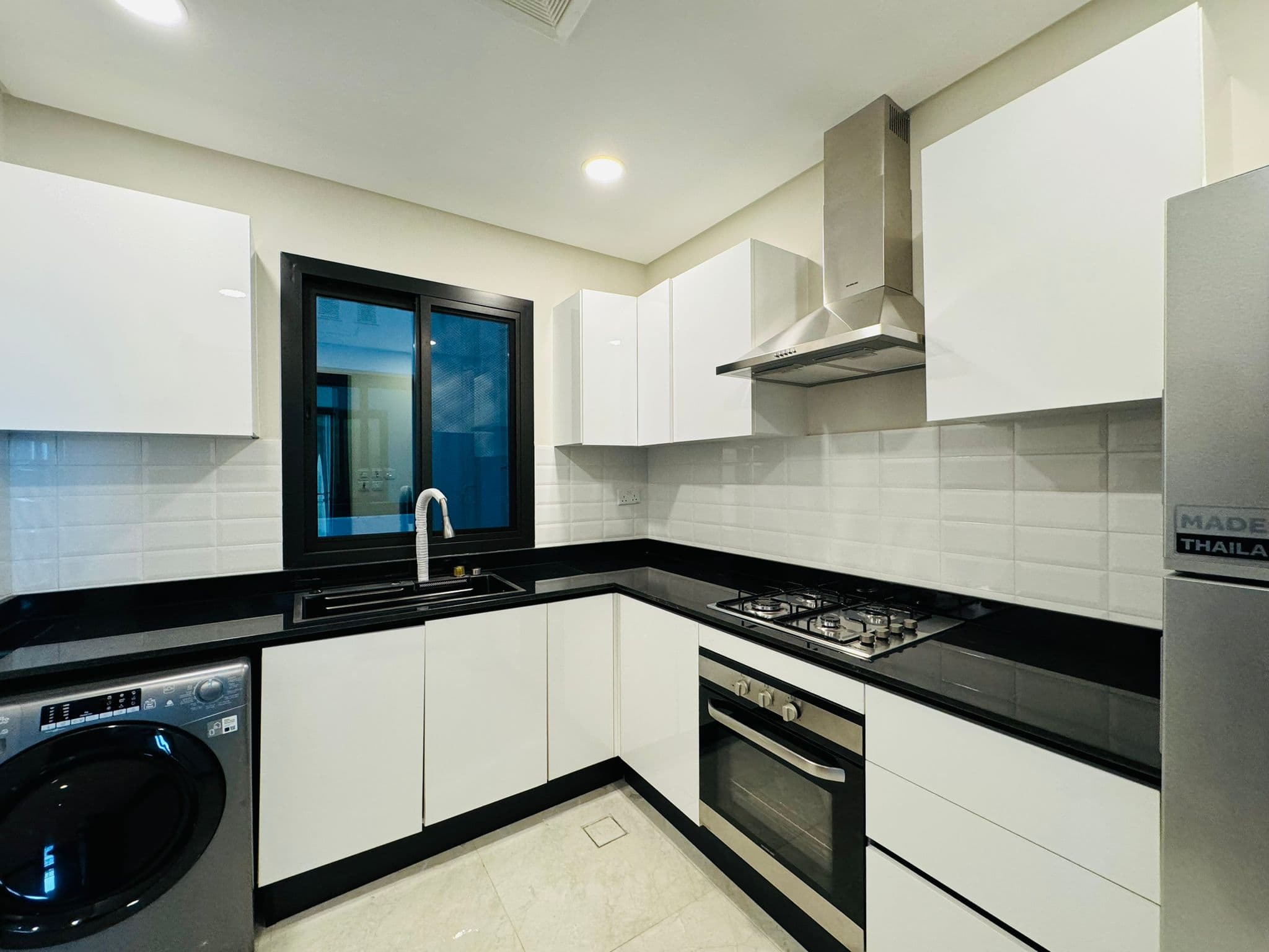 Modern kitchen with white cabinets, black countertops, a window, washing machine, gas stove, oven, and stainless steel range hood.