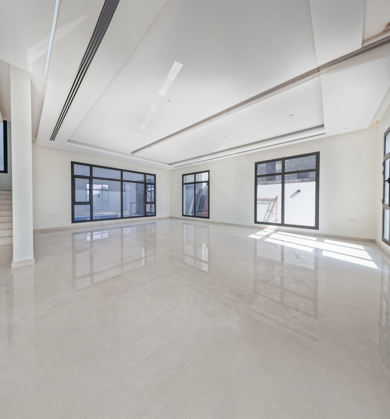 Spacious, empty room with polished marble floor, large windows, and minimalist design featuring recessed ceiling lighting and neutral tones.