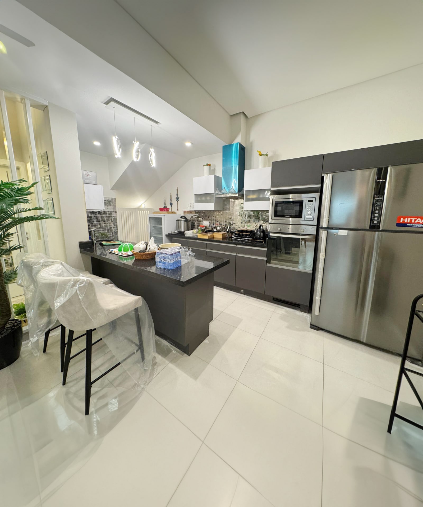 Modern kitchen with stainless steel appliances, black countertops, and bar seating. The room features white cabinetry, a built-in microwave, and a double-door refrigerator.