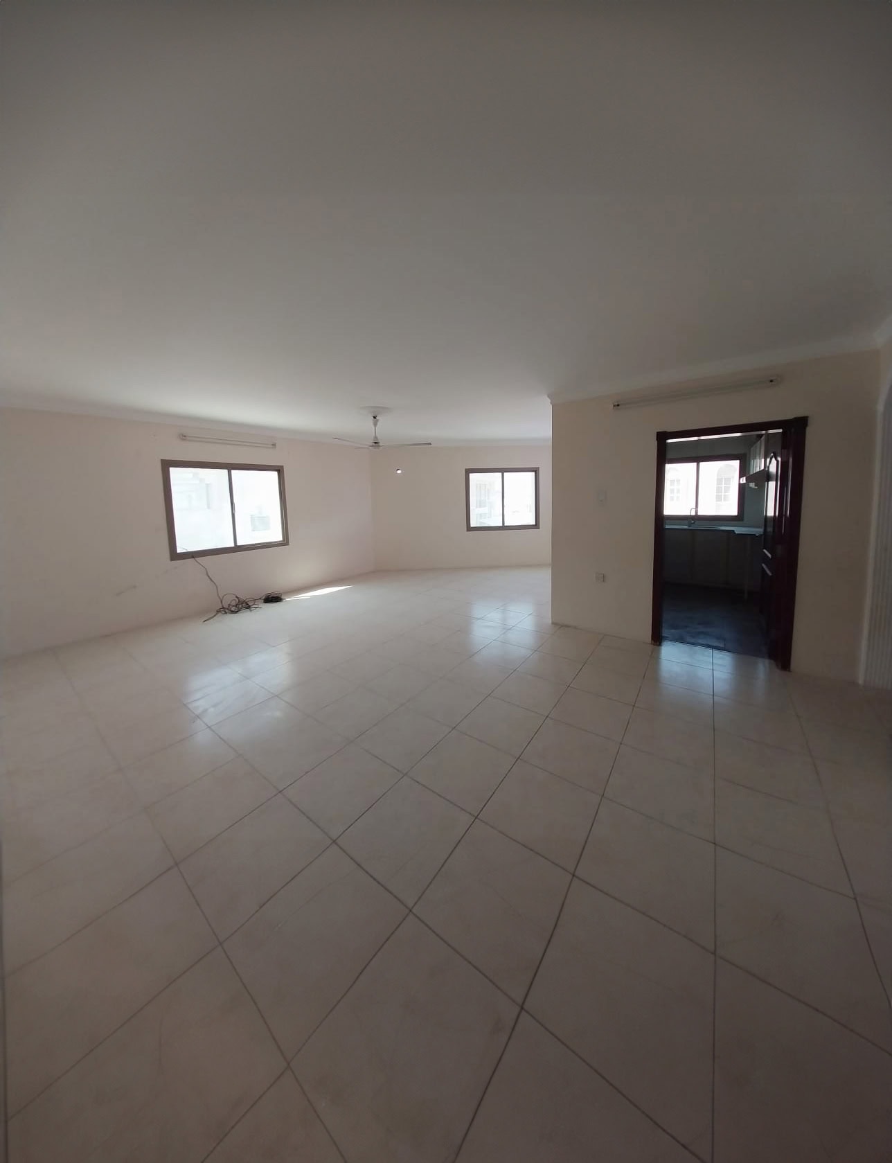 Spacious empty room with tiled floor, white walls, two large windows, and an open doorway leading to another room.