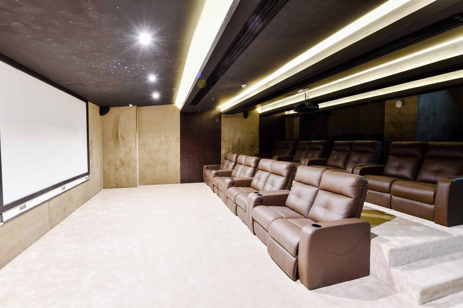 Home theater featuring a large screen, brown reclining seats with cup holders, and ambient ceiling lighting.