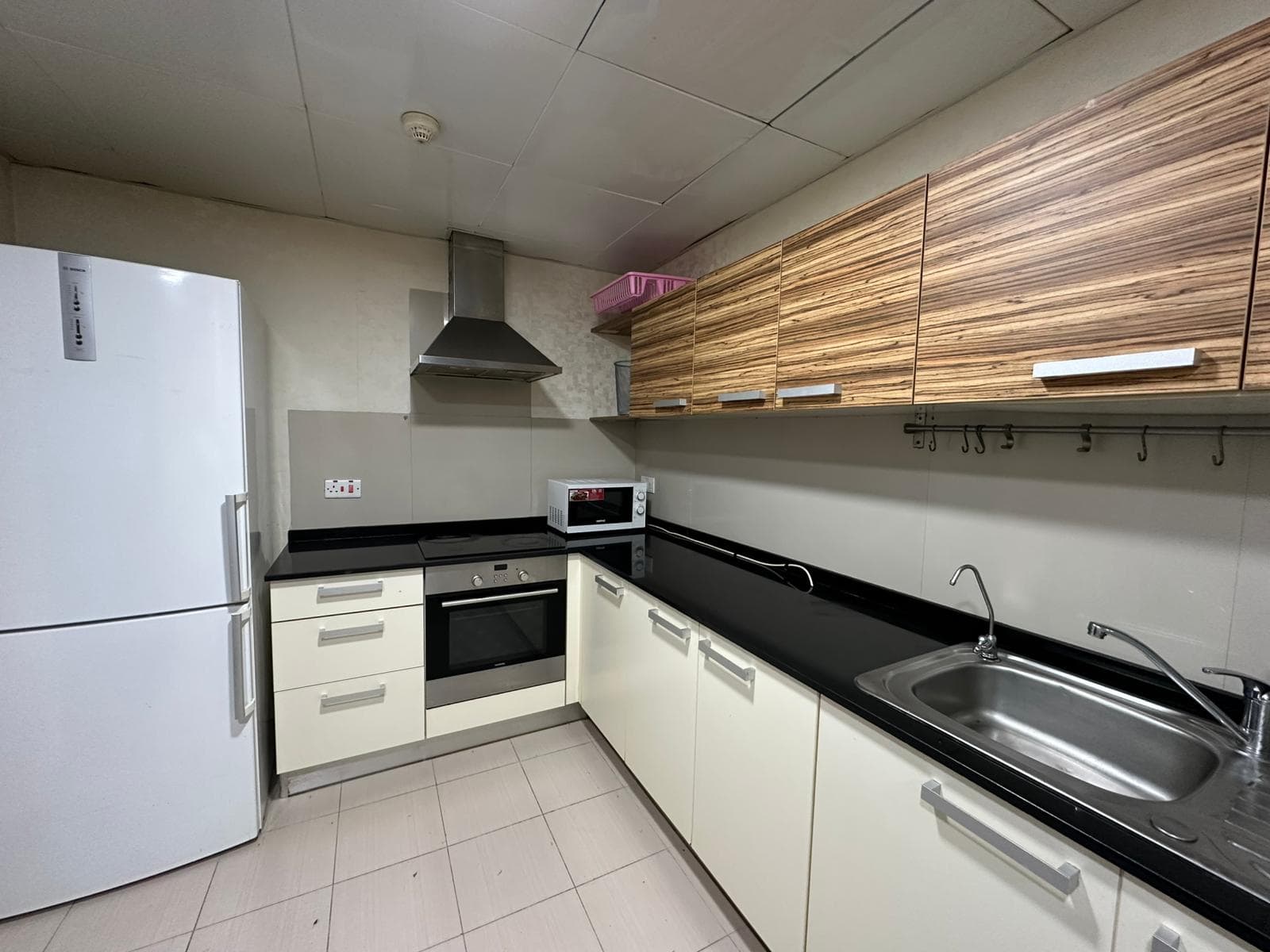 Modern kitchen with white cabinets, black countertop, stainless steel oven, stove, and range hood. White fridge on the left, microwave on the counter, and sink on the right.