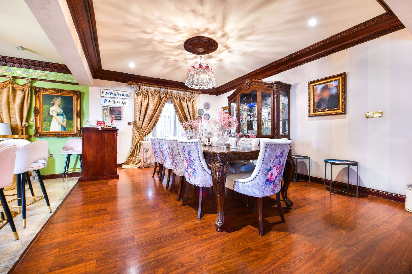 Elegant dining room with floral-patterned chairs around a long table, chandelier overhead, and art-adorned walls.