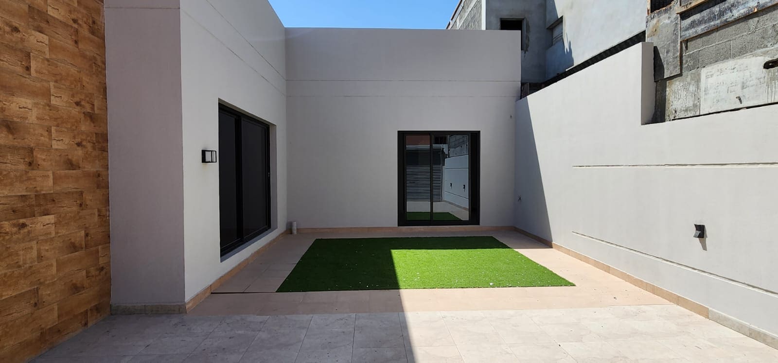 Minimalist courtyard with artificial grass, surrounded by white walls and two large glass doors.