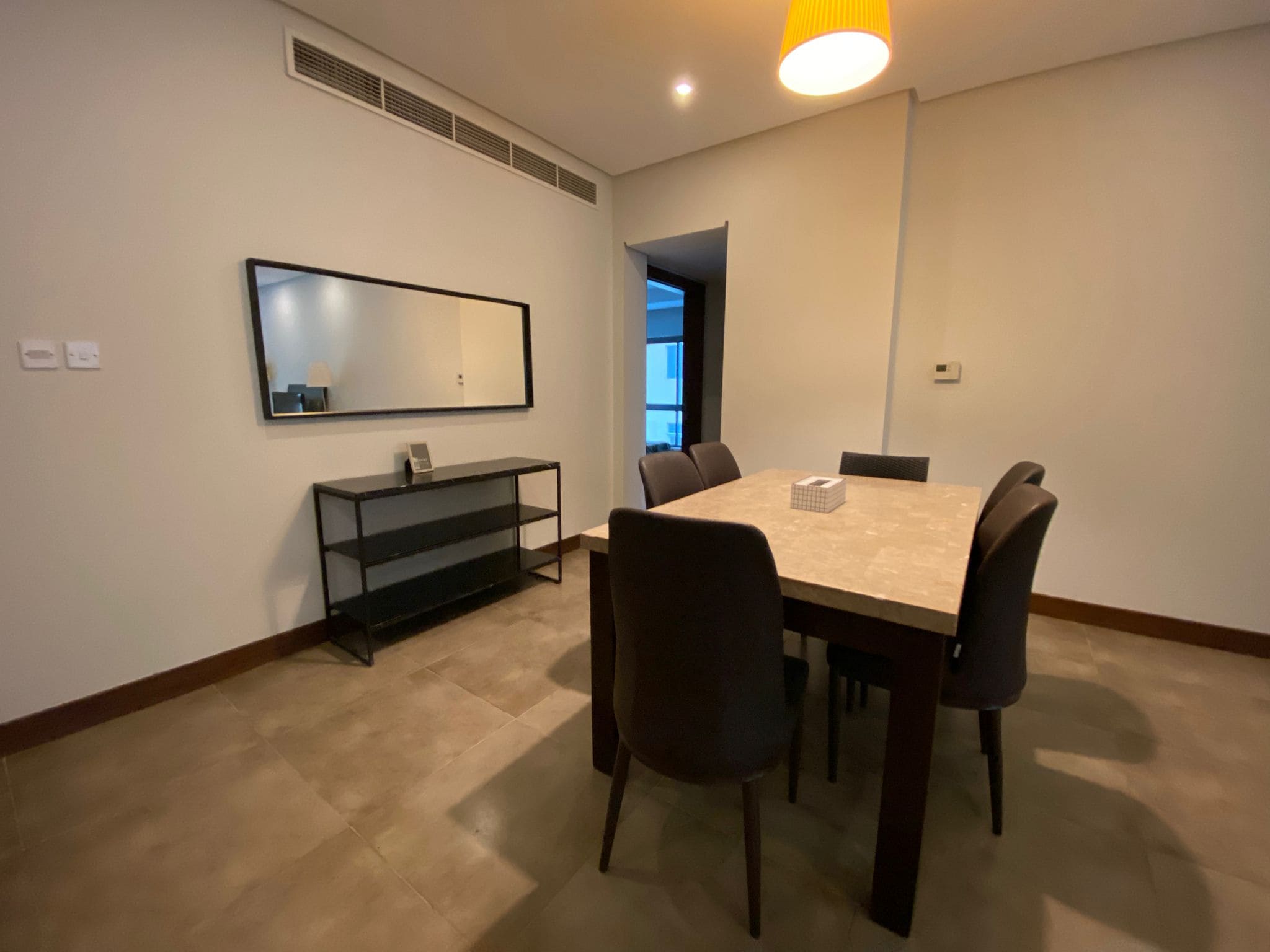 A modern dining room with a table, six chairs, a wall mirror, and a console table under warm lighting.