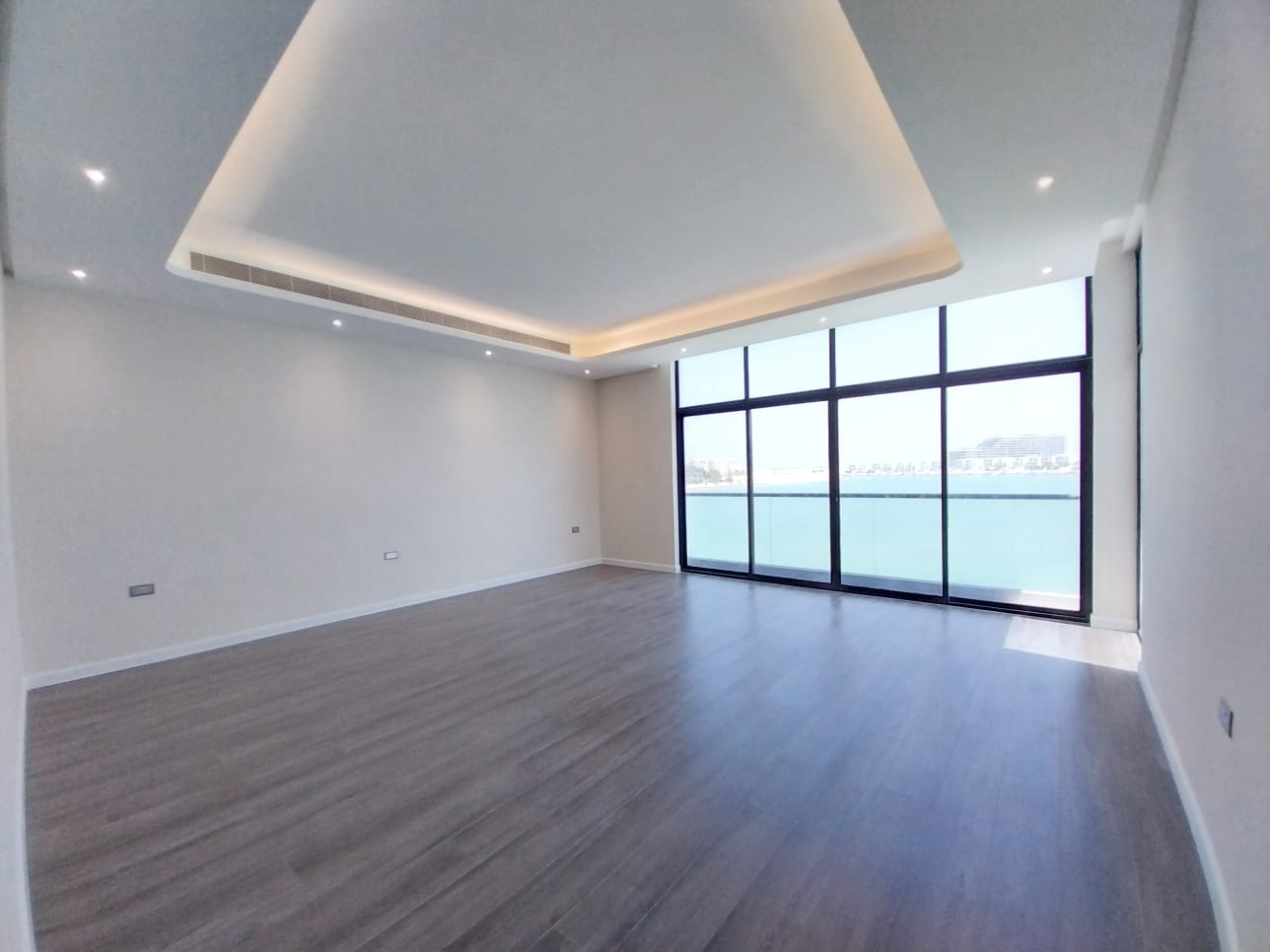 Spacious empty room with wood flooring and large floor-to-ceiling windows offering a view of water and distant landscape. Ceiling features recessed lighting.